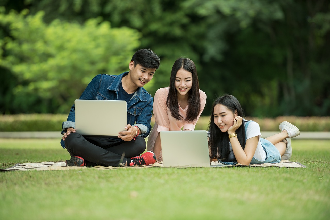 Three students sitting on a lawn, looking at laptops.