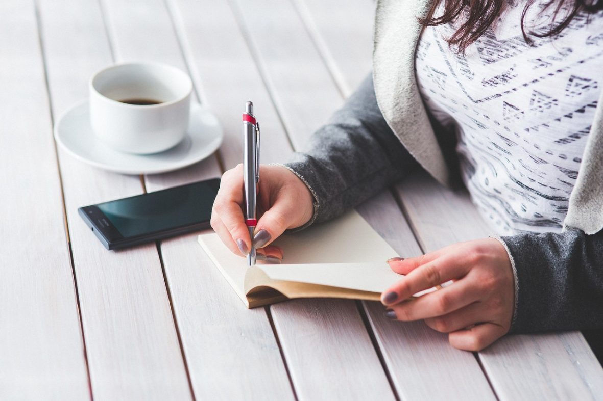 Woman at table writing with a pen.